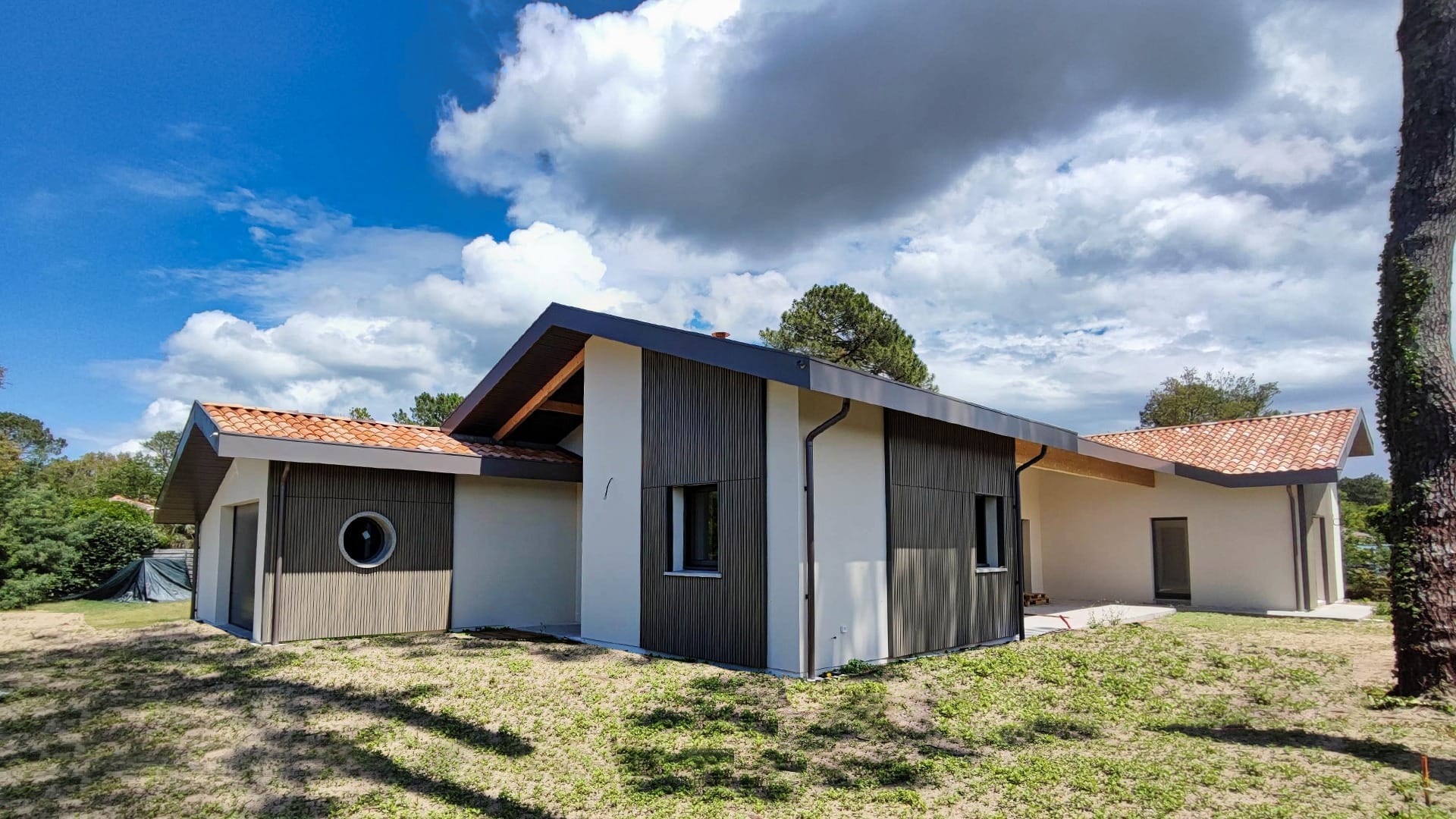 Construction maison Vieux-Boucau : Villa de 174 m² avec 3 suites - Maison Landes Habitat Maison moderne avec un toit en pente et des éléments en bois sur la façade, entourée de verdure.