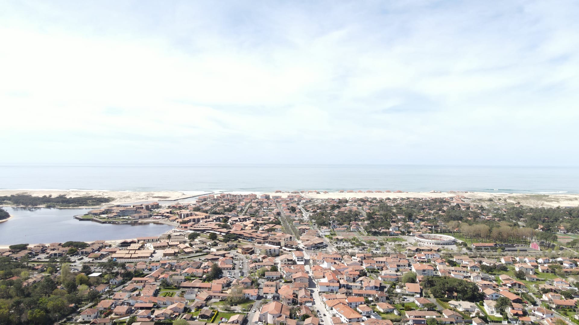 Construction maison Vieux-Boucau : Villa de 174 m² avec 3 suites - Maison Landes Habitat Vue aérienne d'une ville côtière avec des maisons et une plage visible au loin.